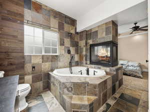 Bathroom with a bath, ceiling fan, toilet, and stone finish flooring