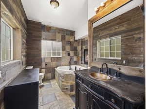 Full bath with a garden tub, toilet, stone finish flooring, wooden walls, and vanity