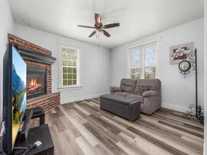 Living area with baseboards, wood finished floors, a brick fireplace, and ceiling fan