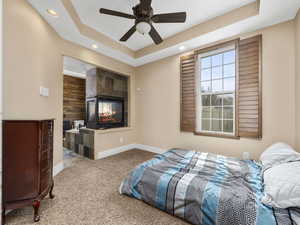 Bedroom with a multi sided fireplace, a raised ceiling, baseboards, carpet flooring, and recessed lighting