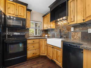 Kitchen featuring dark wood-style floors, a sink, black appliances, and tasteful backsplash