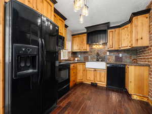 Kitchen featuring a textured ceiling, a sink, tasteful backsplash, dark wood-type flooring, and black appliances