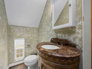 Half bath with wallpapered walls, baseboards, toilet, and vanity