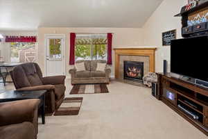 Carpeted great room featuring a vaulted ceiling, a tiled fireplace, and a healthy amount of sunlight