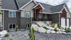 View of front of house with brick siding, a garage, a shingled roof, and stucco siding