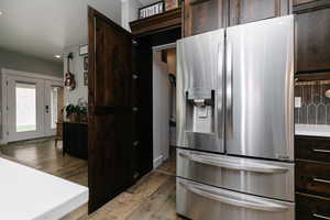 Kitchen with stainless steel fridge, dark brown cabinetry, light wood-type flooring, and recessed lighting