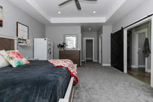 Bedroom with a barn door, a tray ceiling, carpet, a ceiling fan, and recessed lighting