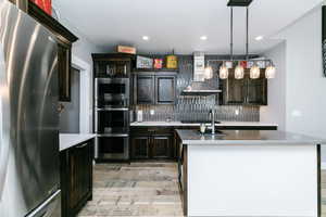 Kitchen featuring appliances with stainless steel finishes, wall chimney range hood, light wood finished floors, backsplash, and light countertops