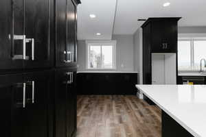 Kitchen with wood finished floors, light countertops, dark cabinetry, freestanding refrigerator, and recessed lighting