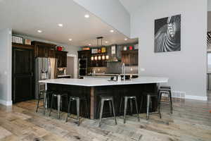 Kitchen featuring wall chimney range hood, appliances with stainless steel finishes, light countertops, a large island, and light wood-type flooring