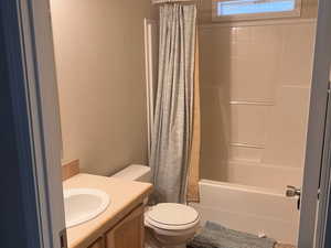 Full bath with shower / bathtub combination with curtain, toilet, a textured wall, and vanity