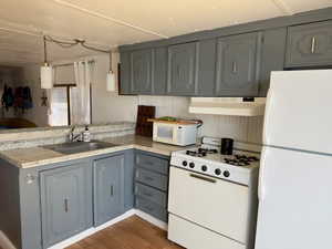 Kitchen with a peninsula, a sink, gray cabinetry, white appliances, and under cabinet range hood