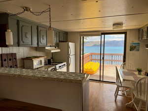 Kitchen featuring under cabinet range hood, wood finished floors, a water view, white appliances, and a peninsula