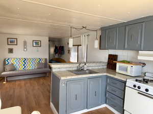 Kitchen featuring a peninsula, wood finished floors, white appliances, and a sink