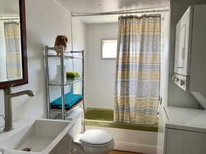 Bathroom with toilet, stacked washer and clothes dryer, a sink, and shower / tub combo with curtain