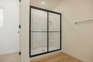 Bathroom with recessed lighting, baseboards, wood finished floors, and a stall shower