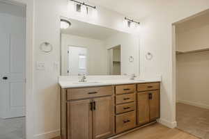 Bathroom featuring double vanity, a spacious closet, baseboards, and a sink