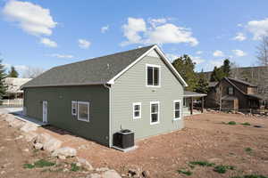 Rear view of property with roof with shingles, central AC unit, and fence