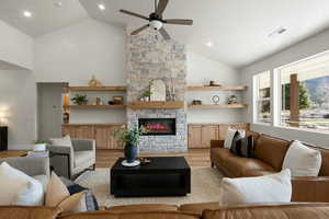 Living area featuring light wood finished floors, visible vents, ceiling fan, a stone fireplace, and high vaulted ceiling