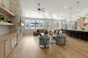 Living area featuring light wood finished floors, lofted ceiling, stairs, ceiling fan, and a stone fireplace