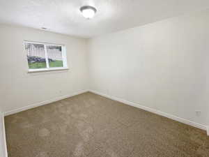 Carpeted spare room with baseboards, a textured ceiling, and visible vents