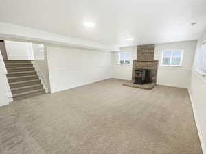 Unfurnished living room with stairway, carpet flooring, a wood stove, and visible vents