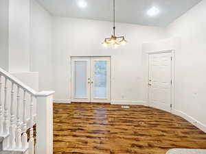 Foyer with baseboards, french doors, wood finished floors, and an inviting chandelier
