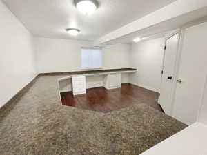 Unfurnished office with dark wood finished floors, built in study area, a textured ceiling, and baseboards