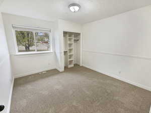 Unfurnished bedroom with a textured ceiling, baseboards, visible vents, carpet, and a closet