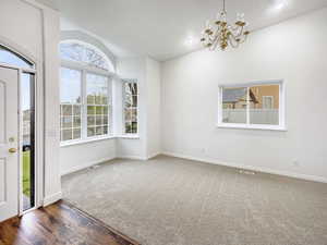Interior space featuring carpet flooring, vaulted ceiling, visible vents, baseboards, and a chandelier