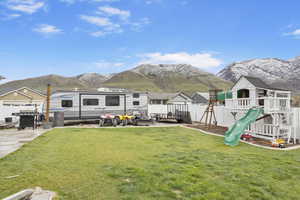 Back of house with fence, a lawn, a mountain view, and a playground
