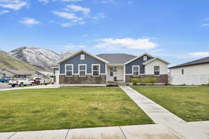 View of front of house with a front lawn, stone siding, board and batten siding, fence, and a mountain view