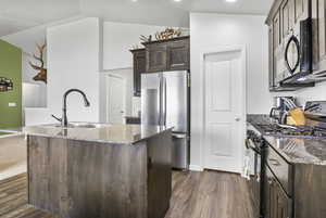 Kitchen featuring dark brown cabinets, dark stone counters, a sink, and black appliances