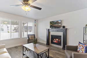 Living area with baseboards, a tiled fireplace, wood finished floors, and a ceiling fan