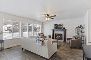 Living area featuring ceiling fan, visible vents, baseboards, a fireplace, and dark wood-style flooring