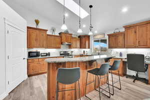Kitchen with lofted ceiling, light wood finished floors, black microwave, a kitchen island, and gas range