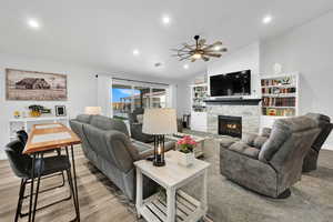 Living room featuring recessed lighting, vaulted ceiling, wood finished floors, a stone fireplace, and ceiling fan