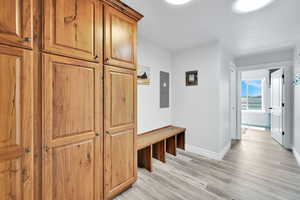 Mudroom with light wood-type flooring, electric panel, and baseboards