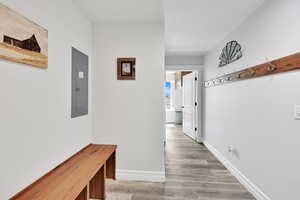 Corridor featuring light wood-style flooring, electric panel, and baseboards