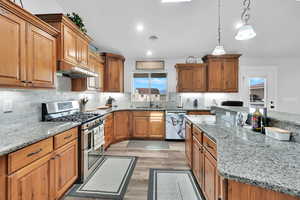Kitchen featuring light wood-style flooring, a sink, visible vents, under cabinet range hood, and appliances with stainless steel finishes