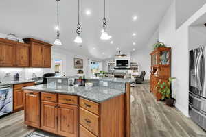Kitchen featuring a center island, light wood-style flooring, a ceiling fan, a fireplace, and appliances with stainless steel finishes