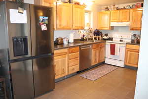 Kitchen with dark countertops, a sink, light brown cabinetry, stainless steel appliances, and under cabinet range hood