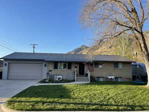 View of front of home with a front lawn, concrete driveway, an attached garage, a mountain view, and metal roof