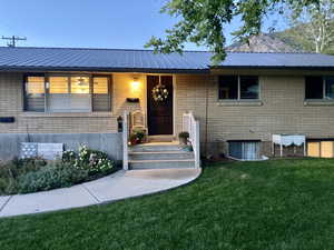 View of front facade featuring a front lawn, brick siding, and metal roof