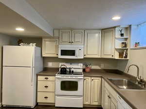 Kitchen featuring cream cabinetry, a sink, white appliances, and recessed lighting