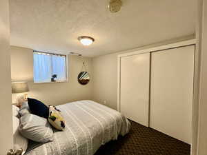 Bedroom with a closet, a textured ceiling, carpet flooring, and visible vents