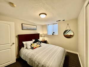 Bedroom with baseboards, dark colored carpet, visible vents, and a textured ceiling