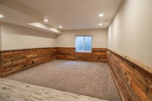 Basement with wood finished floors, a wainscoted wall, carpet, wood walls, and recessed lighting