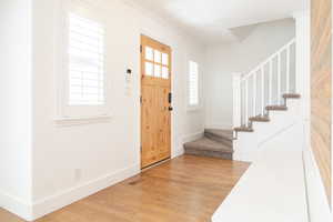 Entryway with stairway, crown molding, light wood-type flooring, baseboards, and visible vents