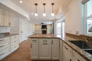 Kitchen with dark stone counters, wood finished floors, ceiling fan, a fireplace, and a peninsula